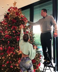 a man and woman are decorating a christmas tree with red flowers on the top