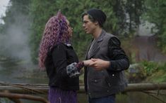 a man and woman standing next to each other in front of a pond with steam rising from the water