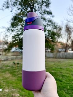 a hand holding a purple and white insulated water bottle