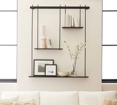 a living room with white couches and two shelves on the wall, one holding books