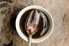 a spoon filled with liquid sitting on top of a white bowl next to a wooden table