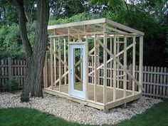 a small wooden structure sitting next to a tree in a yard with a fence around it