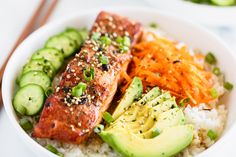 a white bowl filled with rice, salmon and veggies next to chopsticks