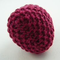 a red crocheted ball on a white surface with one end facing the camera