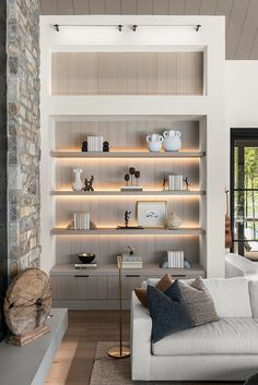 a living room filled with lots of furniture next to a stone wall mounted shelf covered in books