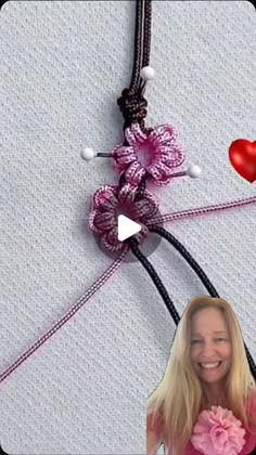 a woman holding a pink flower in front of a wall with two red hearts hanging from it