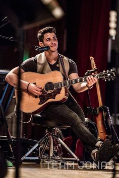 a man sitting on top of a chair holding a guitar in his hand and singing into a microphone