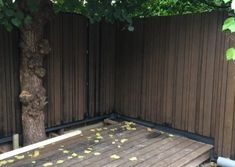 a wooden deck in front of a tree with leaves on the ground next to it