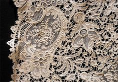 an intricately designed piece of lace on a black background with white flowers and leaves