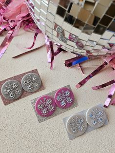 three pairs of pink and silver earrings sitting on top of a white floor next to a mirror