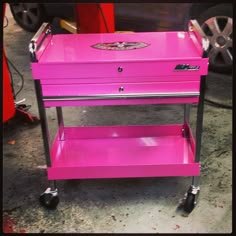 a pink cart sitting on top of a floor next to a car