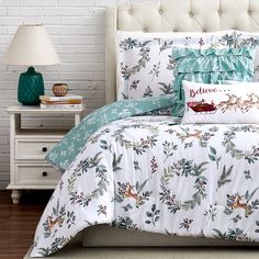 a bed with white and green comforter next to a lamp on a nightstand in front of a brick wall