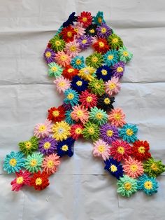 a multicolored crocheted scarf with flowers on it sitting on top of a white sheet