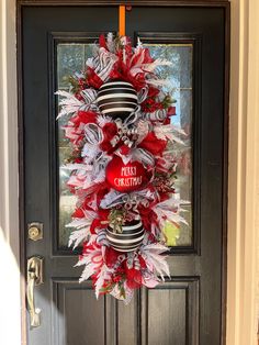 a red and white christmas wreath hanging on the front door with an orange ribbon around it