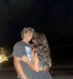 a young man and woman standing next to each other in front of a house at night