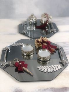 two silver trays with red bows and candles in them on a white table top