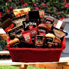 a picnic basket filled with snacks and condiments sits on a bench in the grass