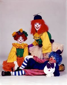 three clowns sitting on the ground posing for a photo