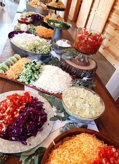 many plates of food are lined up on a long table, with salads and condiments