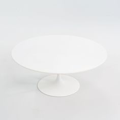 an oval white table with a circular base on a plain surface, in the shape of a tulip