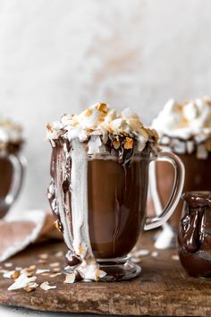 two mugs filled with hot chocolate and whipped cream on top of a cutting board