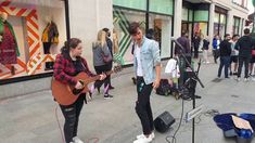 two people are playing guitar and singing on the street