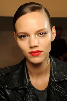 a woman with red lipstick on her face and wearing a black leather jacket is looking at the camera