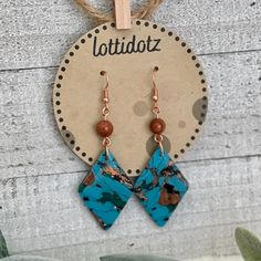 two blue and brown earrings hanging from a wooden hanger on a white wall next to a potted plant