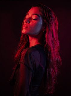 a woman with long hair standing in front of a red light and looking up at the sky