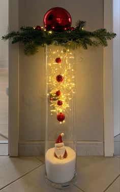 a lighted candle in a glass vase with christmas decorations on the top and around it