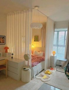 a bedroom with a bed, desk and window in the corner that has sheer curtains on it