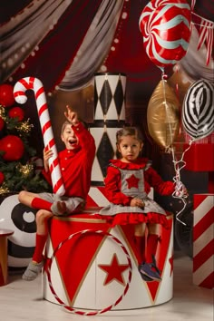 two children sitting on top of a giant candy cane in front of a christmas tree