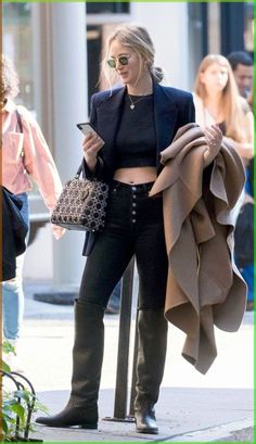 a woman in black is standing on the street with her handbag and looking at her cell phone