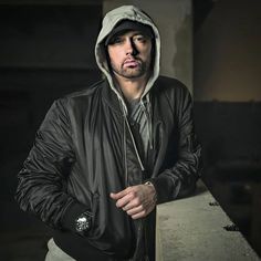 a man with a hoodie on standing in front of a wall and looking at the camera