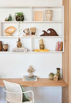 a white shelf filled with books and vases on top of a wooden table next to a chair