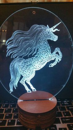 a glass plate with a unicorn on it sitting on top of a laptop computer next to stacks of wooden coasters