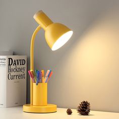 a yellow desk lamp sitting on top of a table next to a book and pine cone