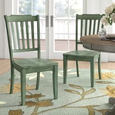 two green chairs sitting on top of a rug in front of a table with flowers