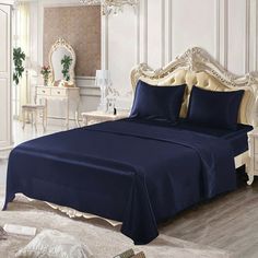 a bed with purple sheets and pillows in a white walled room next to a mirror