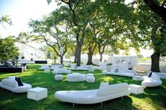 an outdoor seating area with white couches and tables in the middle of it, surrounded by trees