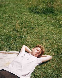 a young man laying on top of a lush green field