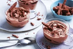 three desserts with chocolate frosting and spoons next to them on a plate