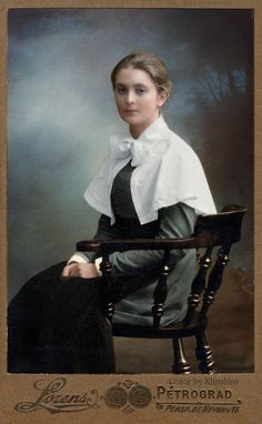 an old photo of a woman sitting in a chair wearing a white blouse and black skirt