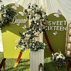 two tall white vases filled with flowers and greenery on top of a grass covered field