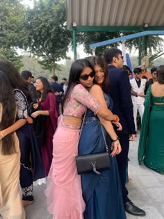 two women hugging each other in front of a group of people wearing sari's