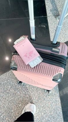 a pink piece of luggage sitting on top of a floor next to a person's feet