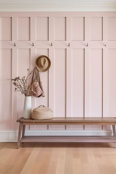 a wooden bench sitting in front of a pink wall with hats on top of it