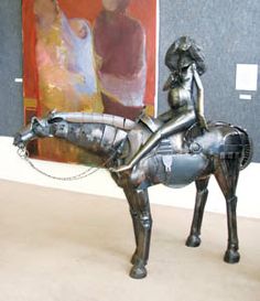 a statue of a woman riding a horse in front of a painting on the wall