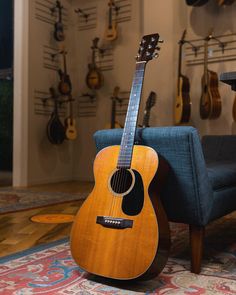 an acoustic guitar sitting on top of a blue chair in front of guitars hanging on the wall