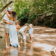 a man and woman hug their children while they stand in the water near some trees